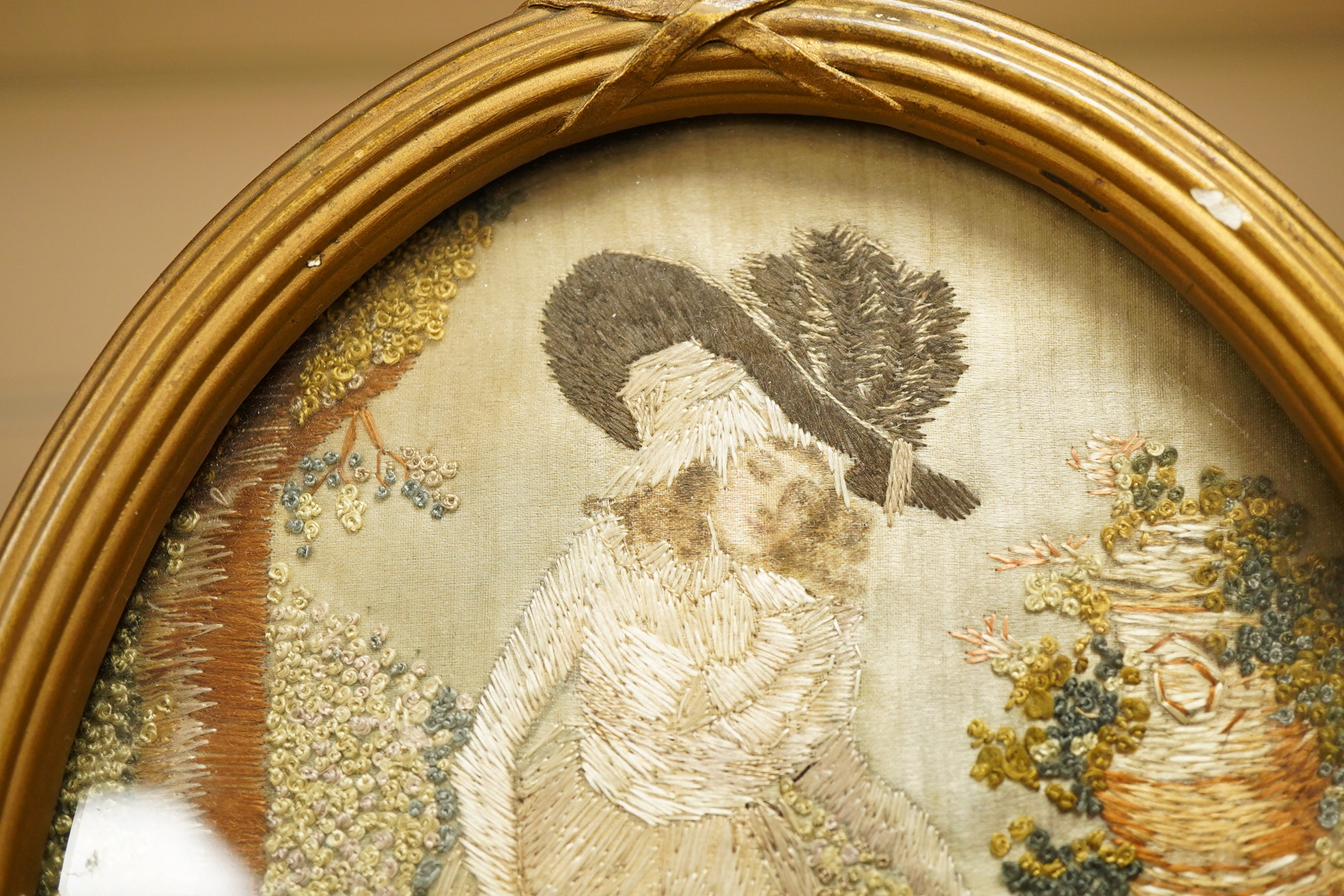 A small oval gilt framed late 19th century silk polychrome embroidery of a lady watering her garden with her dog at her side, 19cm high. Condition - good.